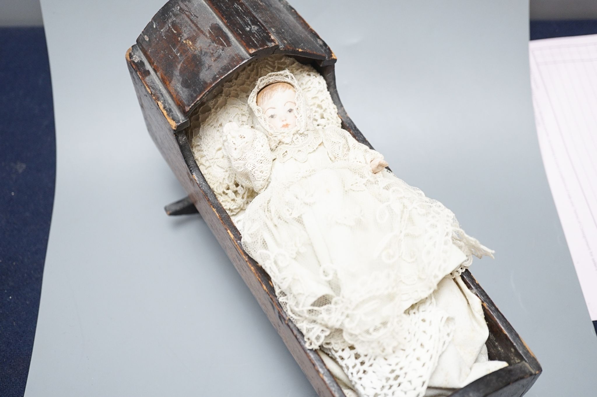 A collection of miniature bisque dolls and another larger doll in a wooden cradle, 11 dolls in total., Cradle 23.5 cms long.